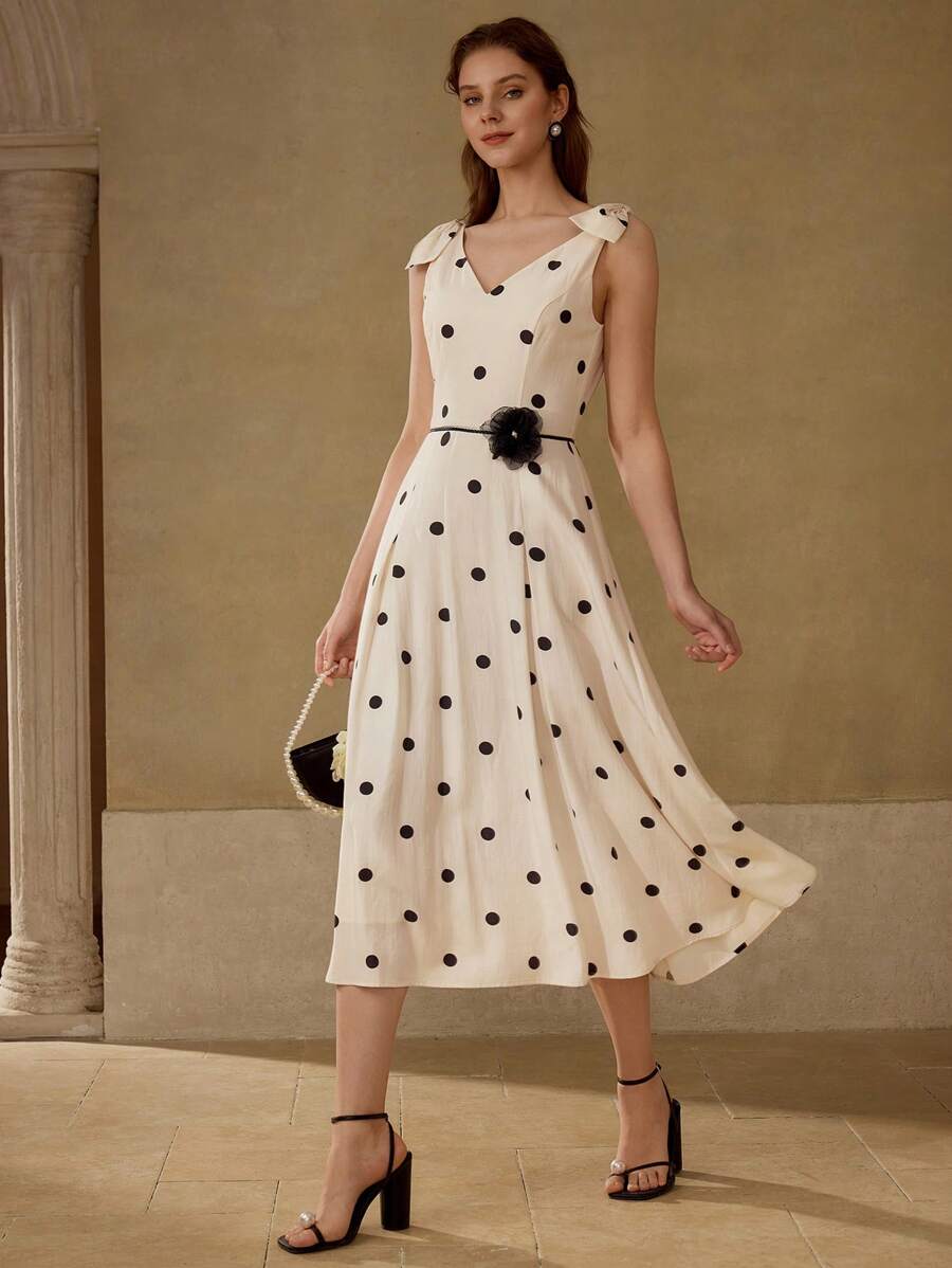 Vestido midi elegante com poás pretos sobre fundo creme e cintura marcada.