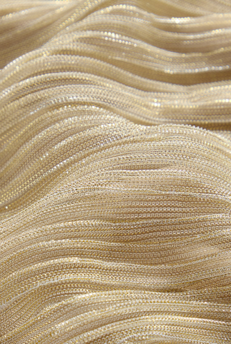 Detalhe aproximado do tecido Dourado Areia com fibras metalizadas e textura finamente plissada.