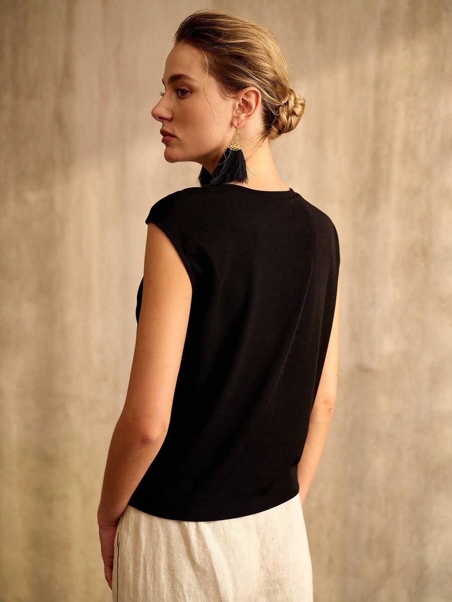 Detalhe do decote assimétrico da blusa feminina preta com pequena fivela metálica decorativa no ombro