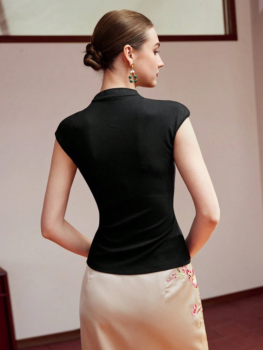 Vista frontal da blusa feminina preta em malha canelada com acabamento em viés e detalhes metálicos no decote